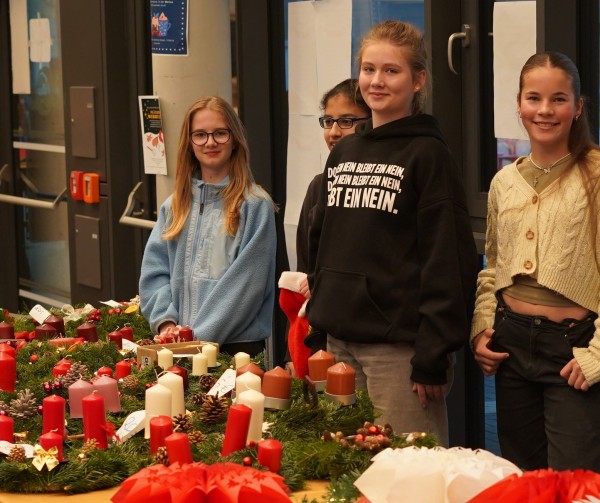 Vier Schülerinnen der siebten Klasse, die stolz ihre Adventskränze präsentieren.