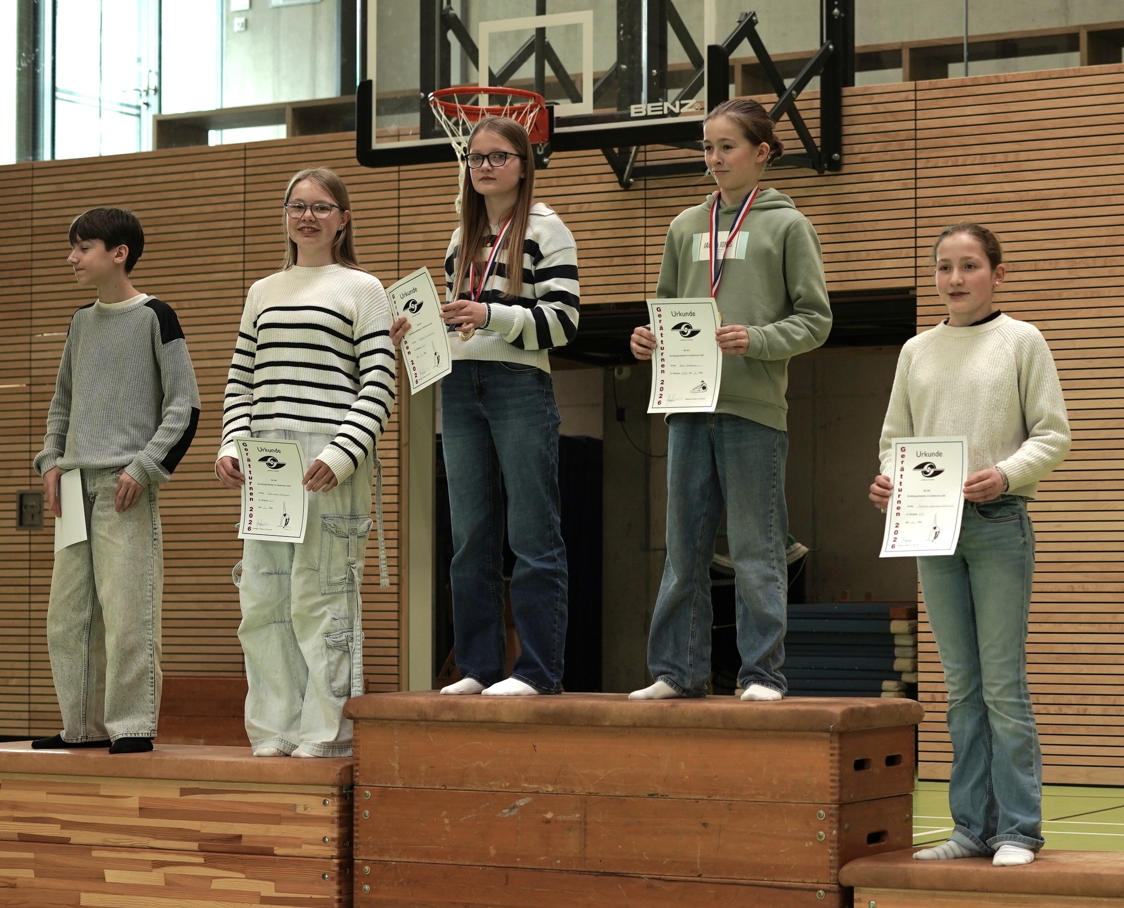 Siegerehrung: Vier Schülerinnen und ein Schüler stehen auf abgestuften Podesten und präsentieren stolz ihre Urkunden